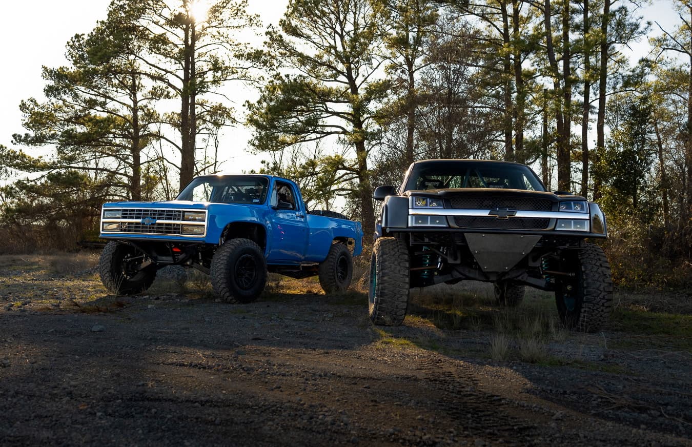Two square body trucks parked in the woods